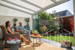 Witte aluminium overkapping aan huis met glazen schuifwanden in de tuin Witte aluminium overkapping aan huis met glazen schuifwanden in de tuin